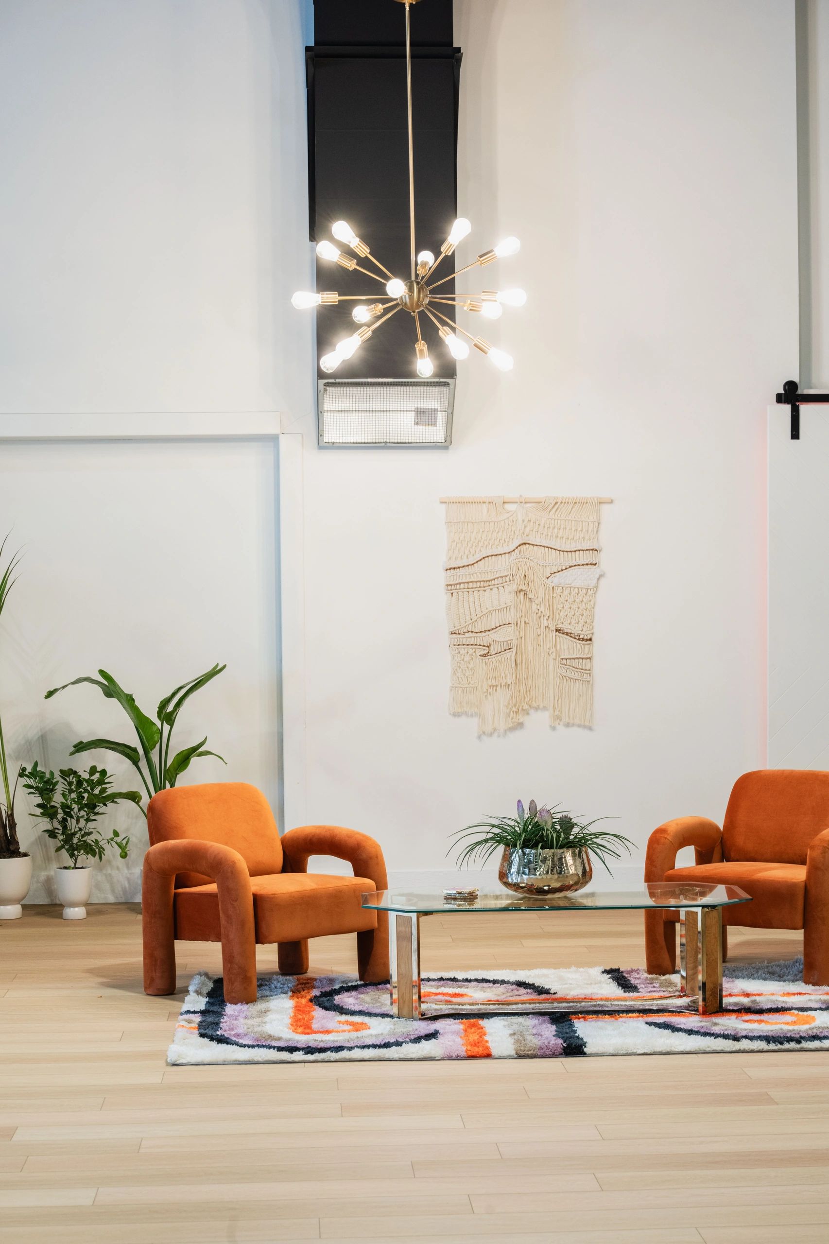 Modern living room with orange chairs, glass table, and decorative lighting.