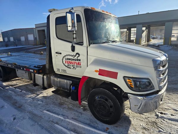White Longhorn Towing truck parked on a snowy surface near garages.