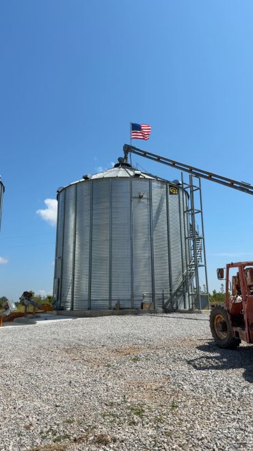 Farm silo with American flag under clear sky.