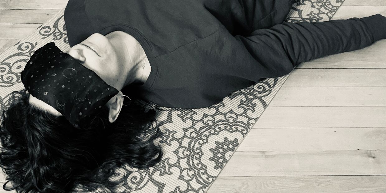Person lying on a patterned yoga mat with an eye mask.