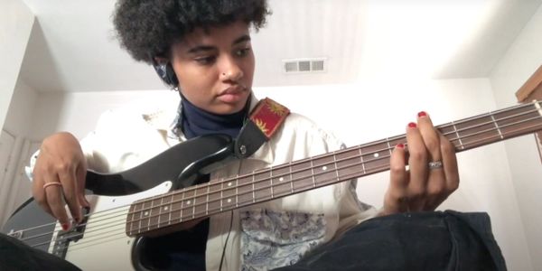 Person focused on playing a black bass guitar indoors.
