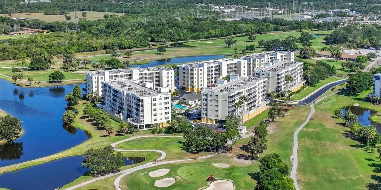 Aerial view of a residential complex surrounded by green golf course and water bodies.