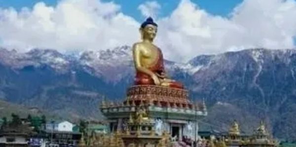 Large golden Buddha statue with snowy mountains in the background.