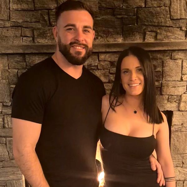 Smiling couple dressed in black posing in front of a stone fireplace.