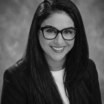 Smiling woman with glasses and long hair in a formal black and white portrait.