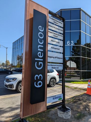 Office sign at 63 Glencoe listing various businesses in a modern glass building.