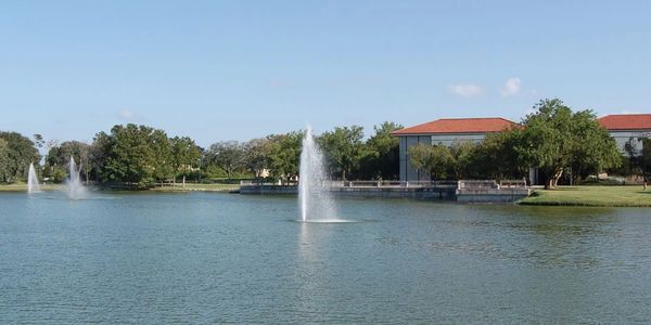 Calm lake with three water fountains under clear blue sky.