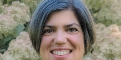 Woman smiling with gray-streaked hair and flowers in the background.