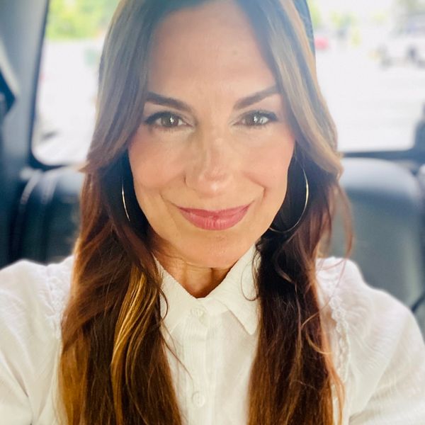 Woman with long hair and hoop earrings smiling inside a car.