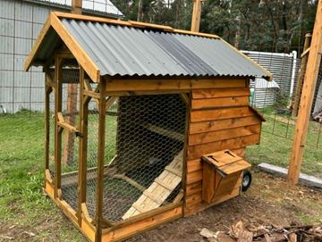 A wooden chicken coop with a wire mesh front and a slanted roof.