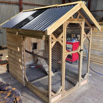 Wooden chicken coop with wire mesh and a corrugated roof indoors.