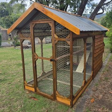 A wooden chicken coop with wire mesh on a grassy lawn.