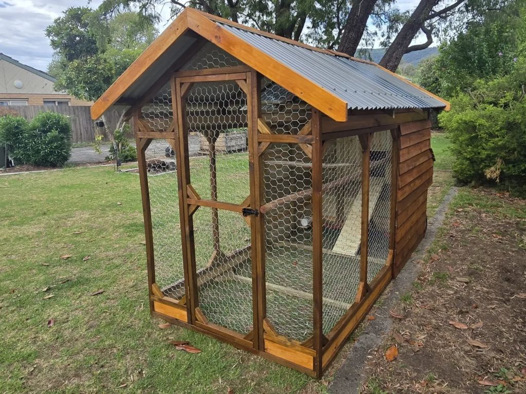 A wooden chicken coop with wire mesh and a metal roof in a backyard.
