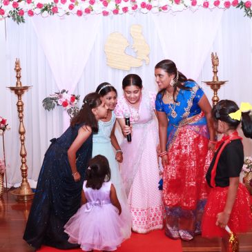 Group of women and children dressed in festive attire at a decorated event stage.