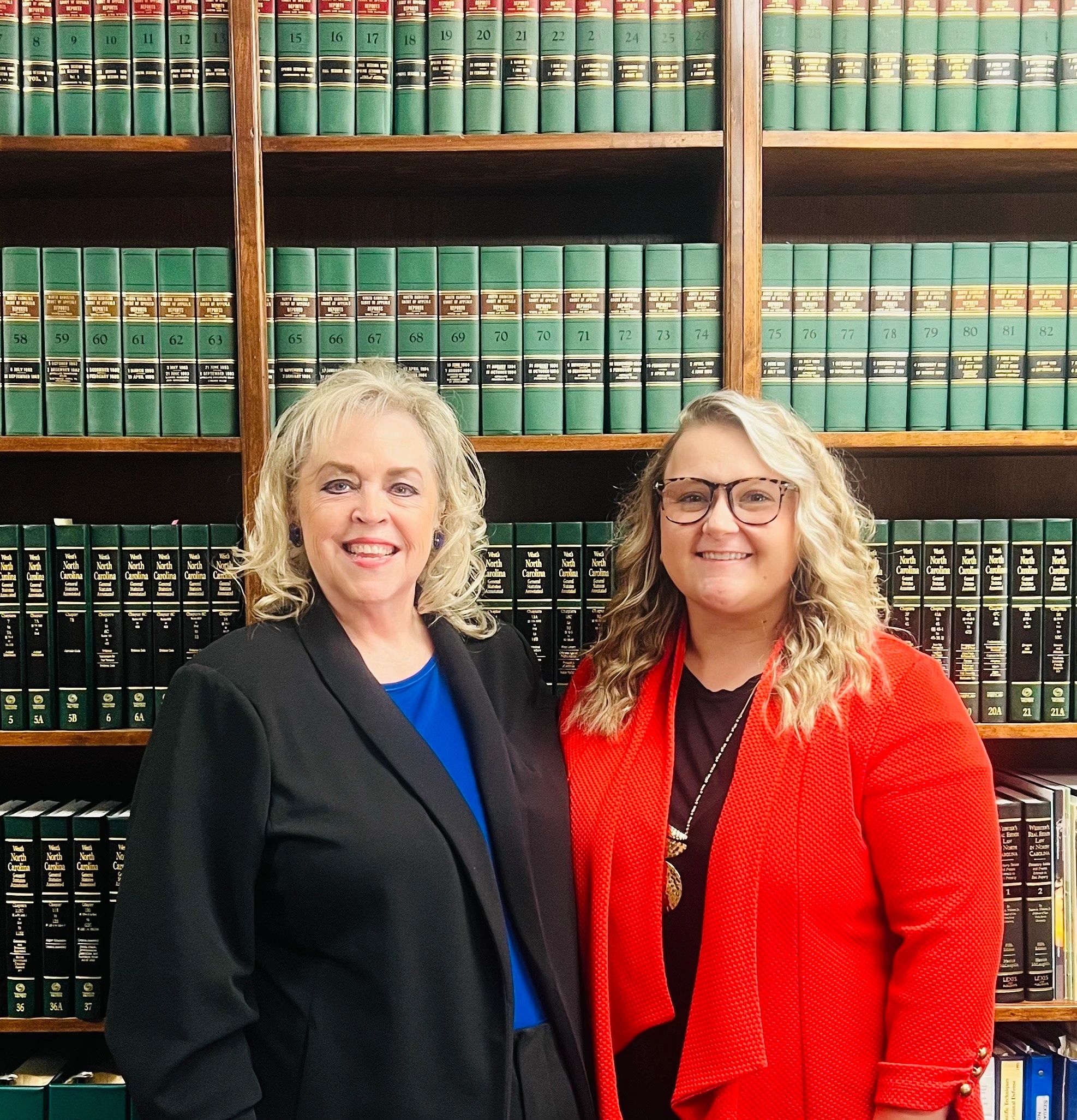 Two professional women smiling in front of law books.