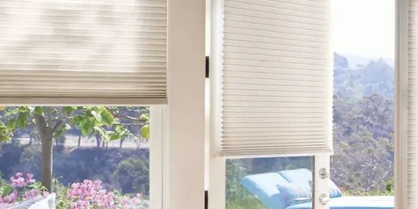 Indoor view of white window blinds with a scenic garden outside.