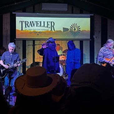 Live band performing on stage at Traveller venue with audience hats visible.