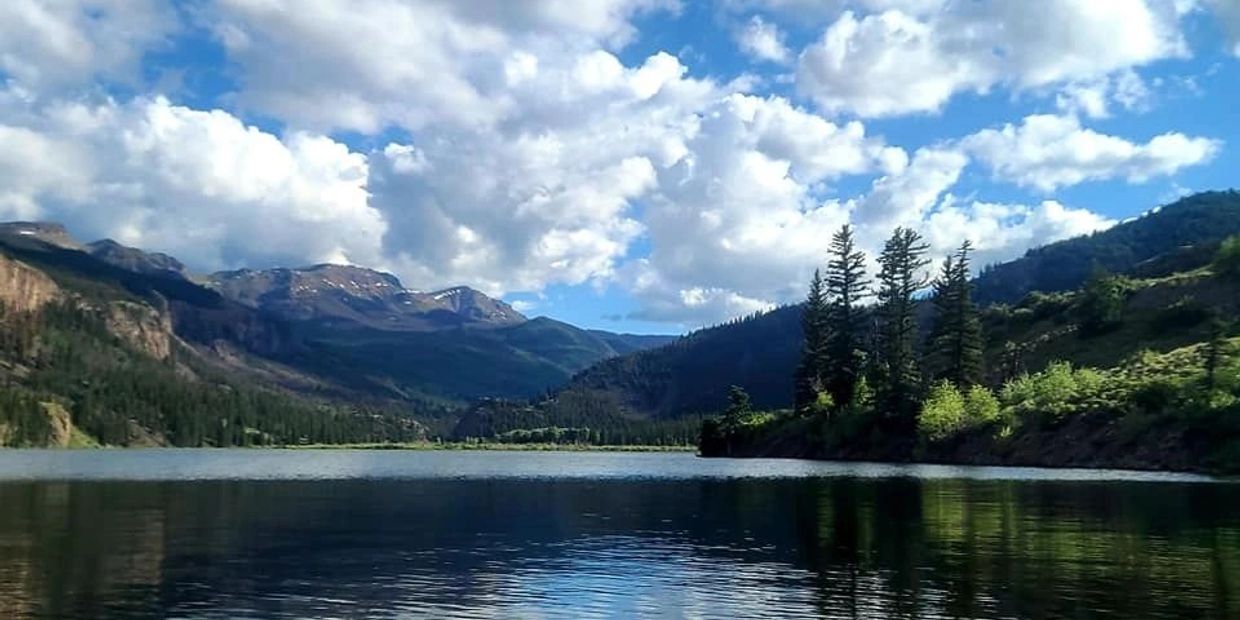 View from a kayak on a calm mountain lake under a partly cloudy sky.