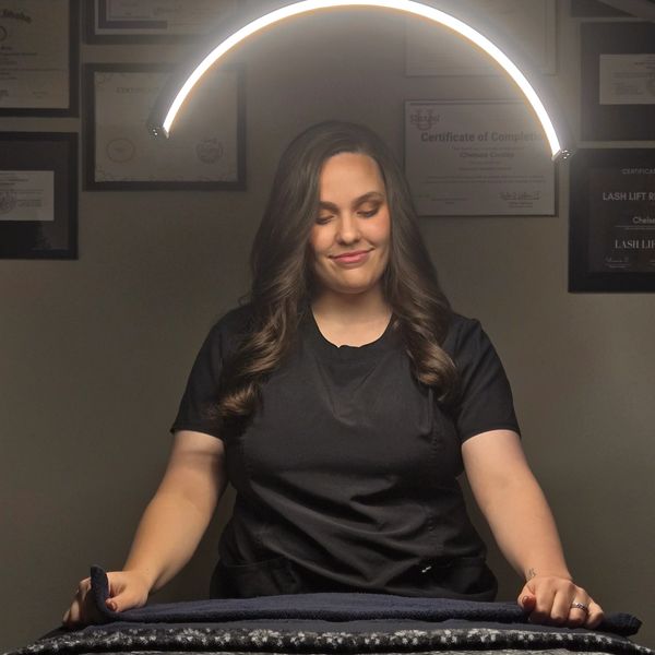 Woman smiling under a glowing half-circle light with certificates in background.