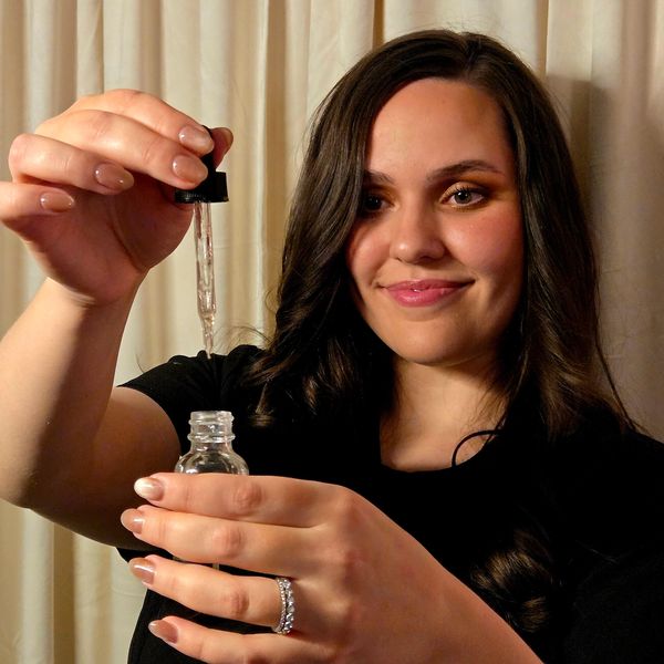 A woman smiling while holding a dropper and bottle.