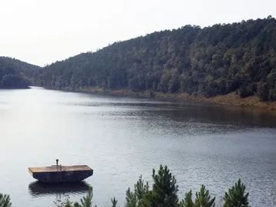 A calm river surrounded by forested hills and a floating platform.