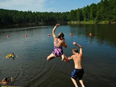 Children jumping into a lake surrounded by forest on a sunny day.