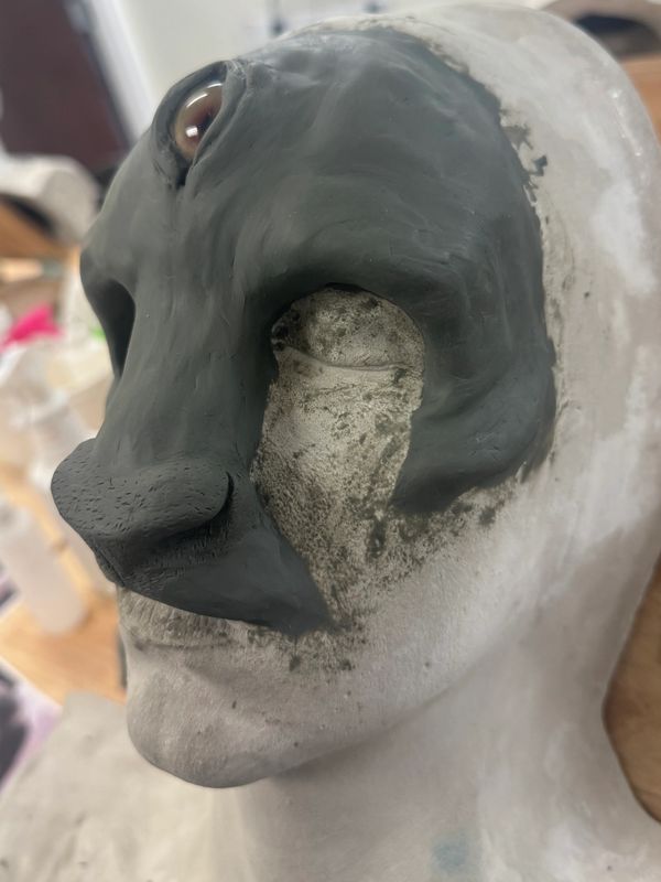 Close-up of a sculpted face with dark clay around the eyes and nose.