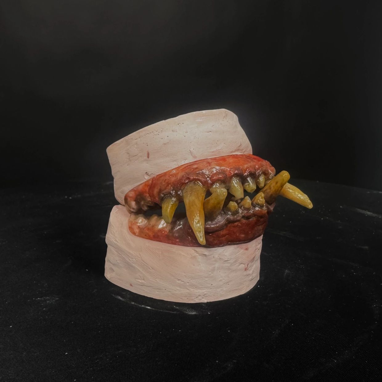 A sculpted model of monstrous teeth with sharp yellow fangs on a dark background.
