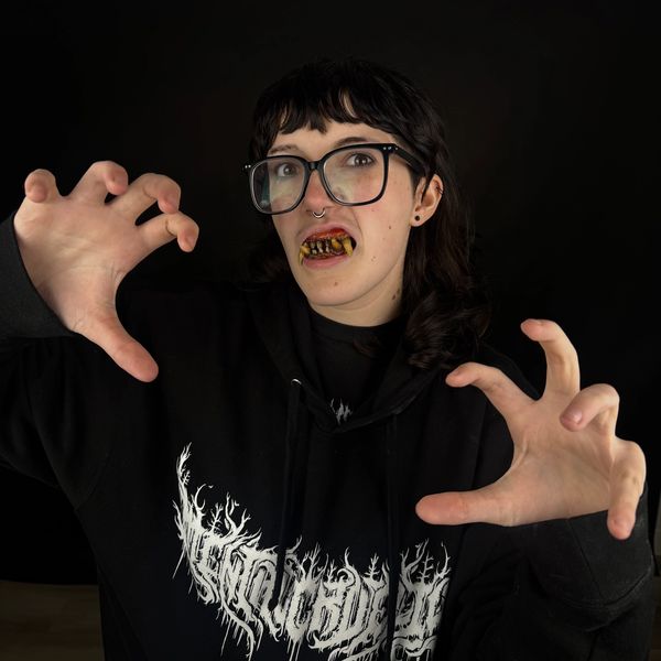 Person with fake monster teeth and glasses striking a scary pose.