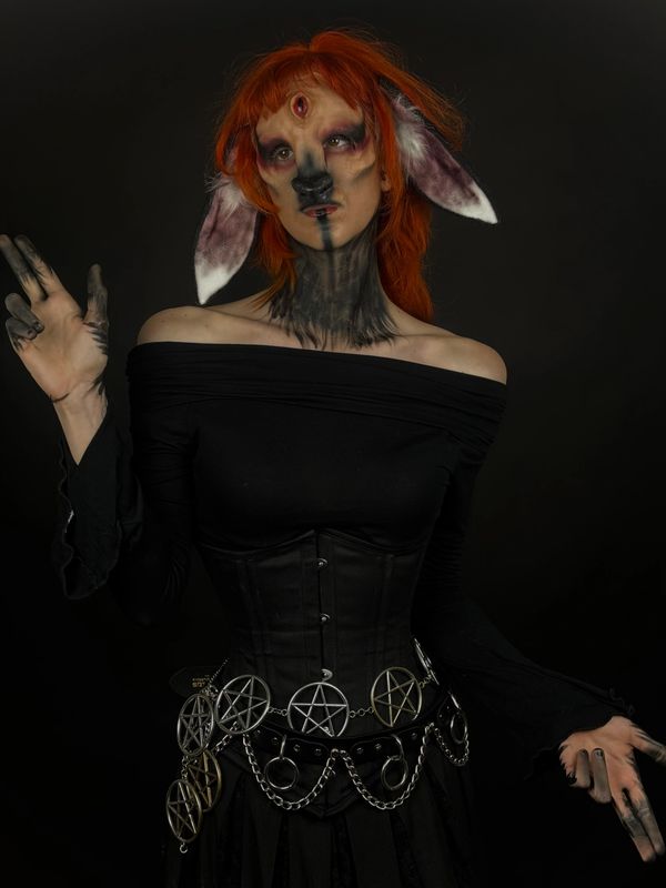Person in dark fantasy makeup with red hair and pentagram belt.