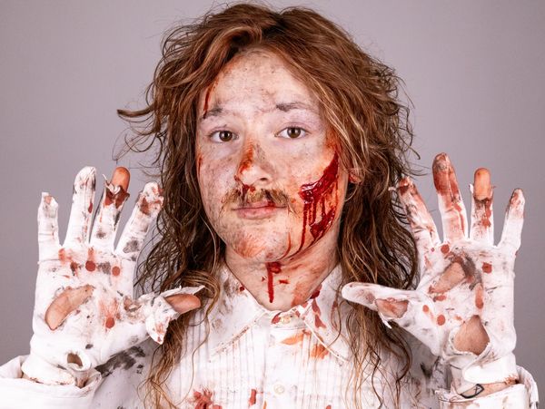 Person with messy hair and blood-stained face and gloves.