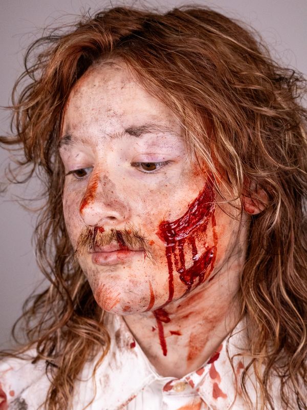 Person with fake blood and makeup resembling injury on face.