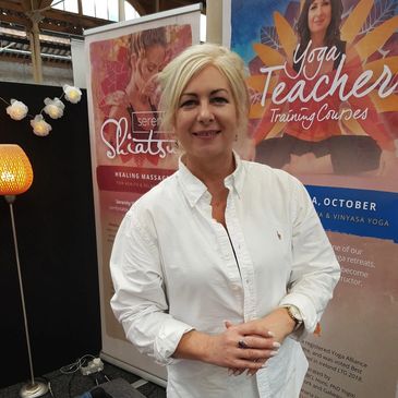 Woman in white shirt smiling at a wellness event with yoga and massage banners.
