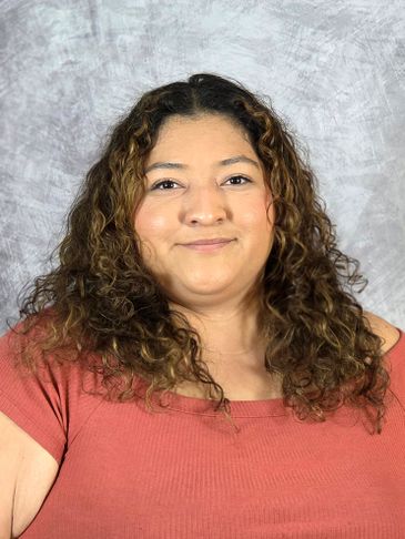 Smiling woman with curly hair in a coral top against a textured gray background.
