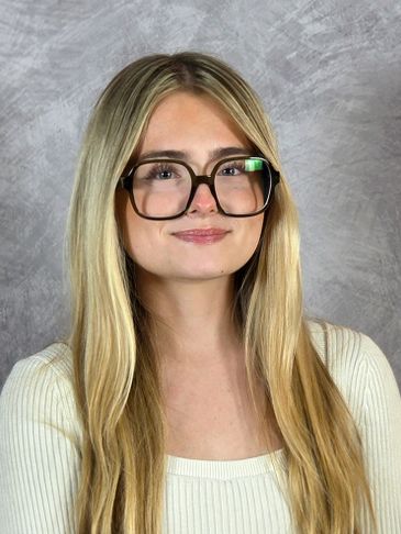 Young woman with long blonde hair and oversized glasses smiles subtly.