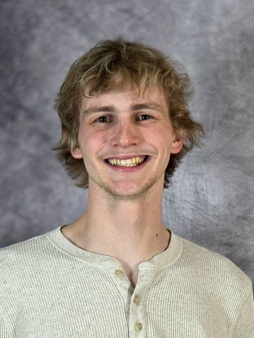 Young man with blonde hair smiling in a casual cream shirt.