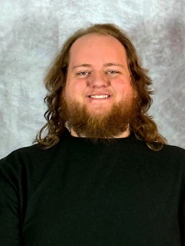Smiling man with long hair and beard wearing black sweater.