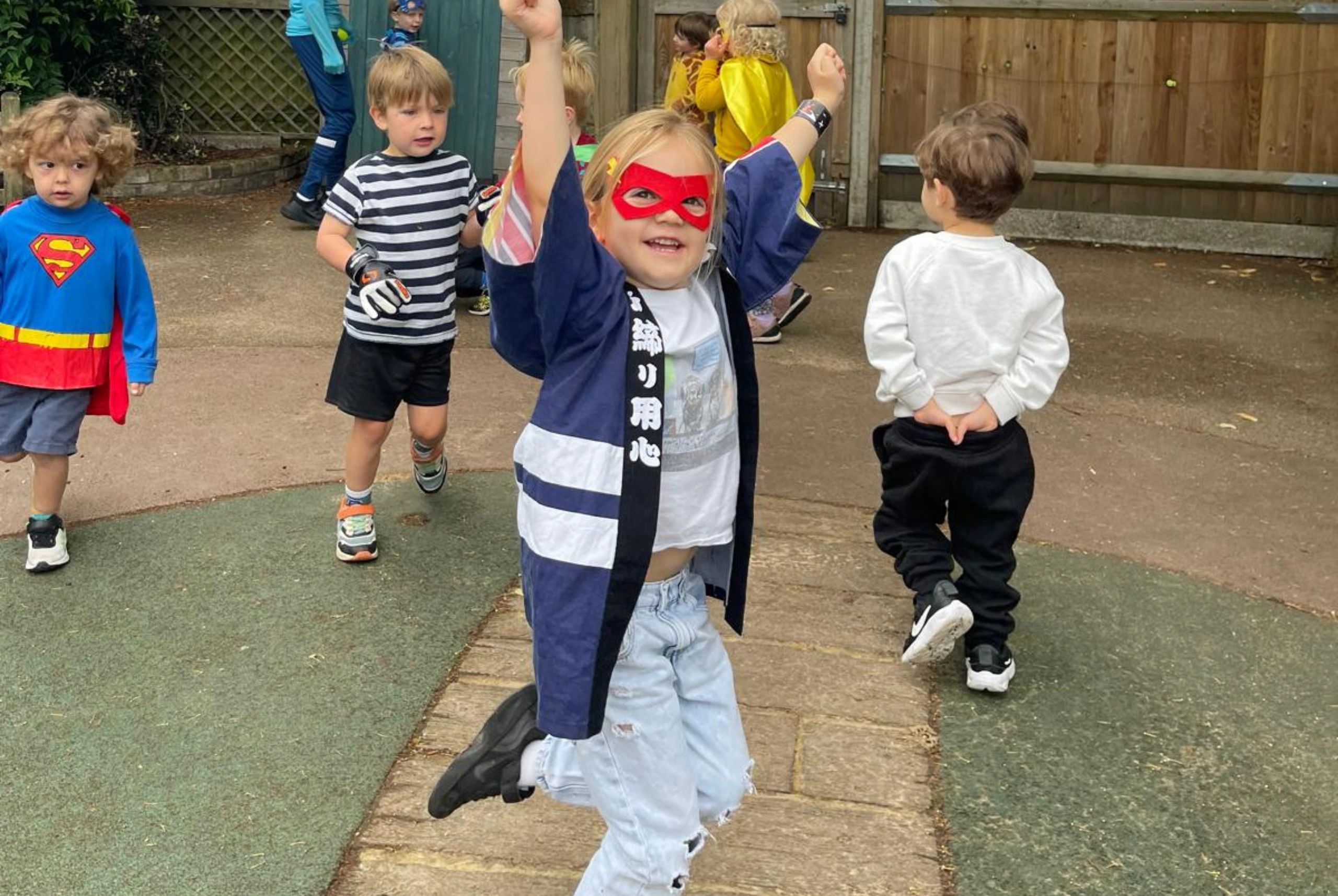 Children in colorful costumes playing outdoors, one jumping joyfully.
