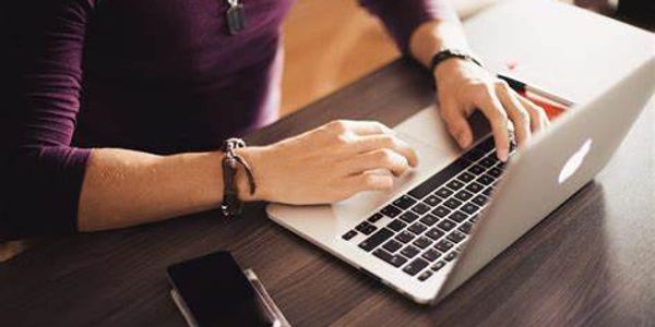 Person typing on a laptop at a wooden desk with a smartphone nearby.