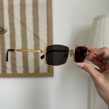 Hand holding stylish gold-framed sunglasses with dark lenses.