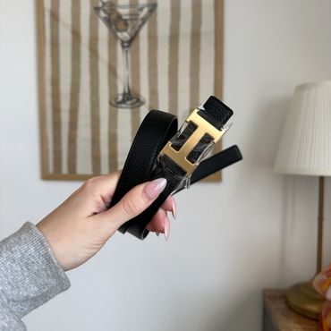 Hand holding a black leather belt with a gold 'H' buckle.