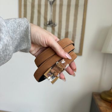 Hand holding a brown leather belt with a silver buckle indoors.