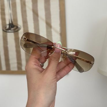 Hand holding stylish brown gradient sunglasses with gold frame.
