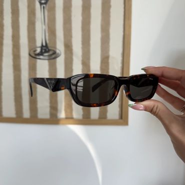 Hand holding rectangular tortoiseshell sunglasses with dark lenses.