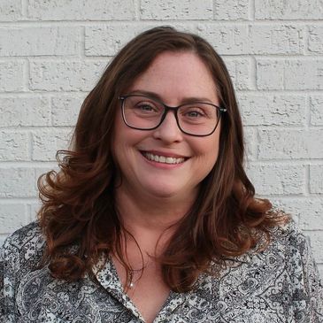 Shannon, massage therapist, smiling by brick wall