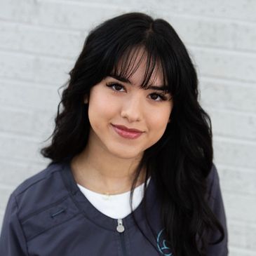 Yessica, esthetician and skincare specialist, smiling by brick wall