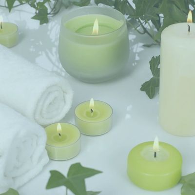 green candles that are lit with towels nearby and greenery