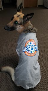 German Shepherd wearing a gray shirt with a 'Respect Our Law Enforcement' emblem.