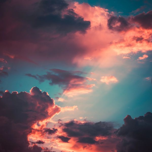 sky at sunset, hues of pink, purple and blue, with the sun shining through clouds.