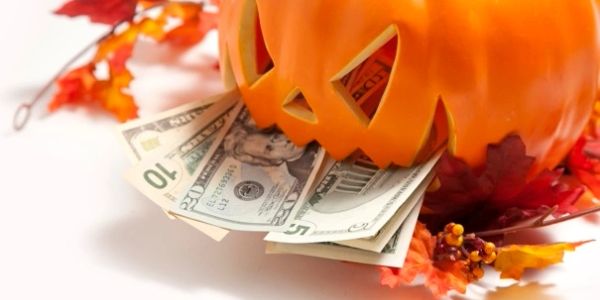 Halloween pumpkin with money sticking out, surrounded by autumn leaves.